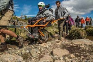 Un joven en silla de ruedas recorriendo un sendero en Torres del Paine, mientras otras personas los ayudan levantando su silla.