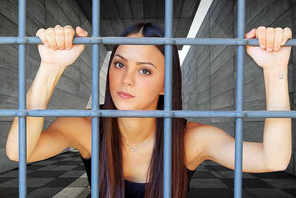 Una mujer aparece dentro de una cárcel en españa afirmada de las rejas y mirando a la cámara.