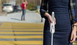 Una mujer cruzando un paso peatonal utilizando un bastón que incluye botones con diferentes funciones.