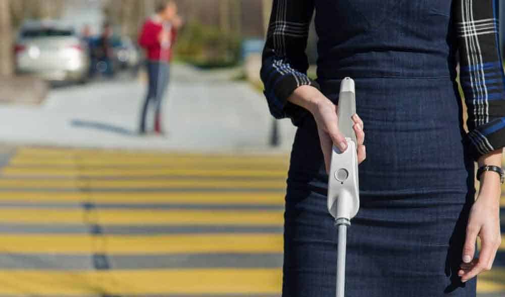 Una mujer cruzando un paso peatonal utilizando un bastón que incluye botones con diferentes funciones.
