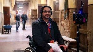 Un hombre en silla de ruedas con audífonos y un guión en la mano durante la grabación de la película "Pacto de Fuga"