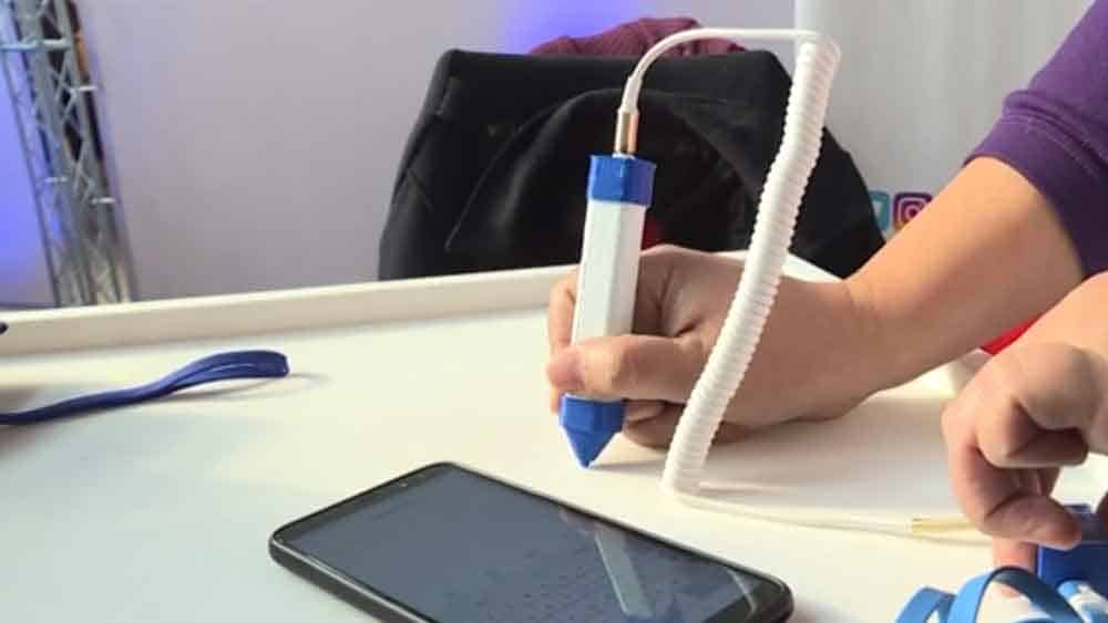 Aparece la mano de una persona escribiendo sobre una tabla con un lápiz especial, y al lado hay un celular donde se va viendo en la pantalla la traducción.