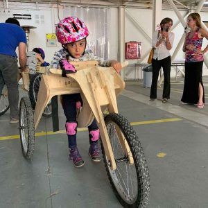 Una niña sobre una bicicleta de madera y con tres ruedas.