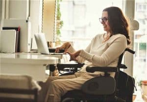 Una mujer en silla de ruedas trabajando en su computador en su casa.