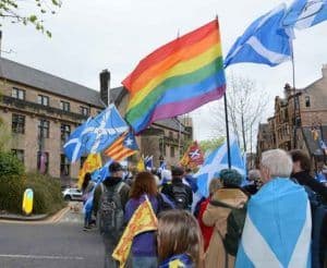 Foto de una manifestación LGBTI en Escocia donde hay personas marchando con banderas del arcoiris con banderas esocesas.