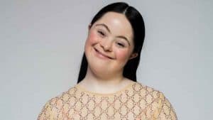 Una modelo con síndrome de Down con un vestido color cafe claro sonríe a la cámara en un estudio fotográfico.