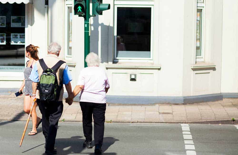 Dos adultos mayores van tomados del brazo mientras cruzan un paso peatonal.