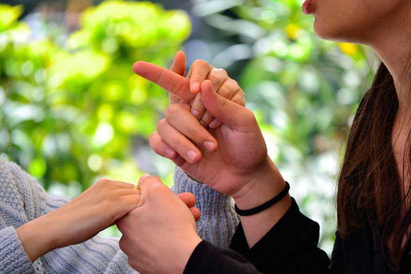 Aparecen las manos de dos personas en contacto directo con la intención de mostrarle una seña a una persona sordociega.