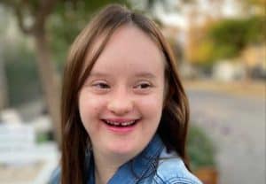 Foto en primer plano de una joven con síndrome de Down sonriendo a la cámara.