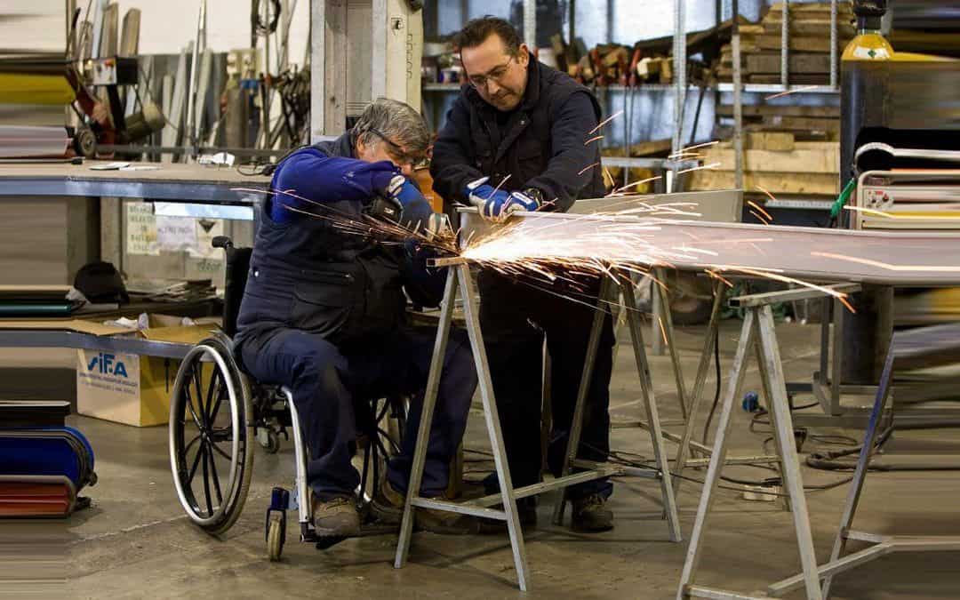 Foto de una persona en silla de ruedas soldando una mesa dentro de un taller.