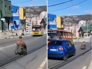 Pantallazo de un video donde aparece una persona en silla de ruedas bajando por una calle en un cerro de valparaíso, y de frente hay una micro y atrás de él viene un auto que lo intenta adelantar.
