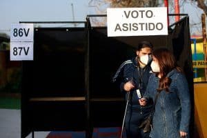 Foto de una persona ciega siendo acompañada por otra persona en la urna de votación.